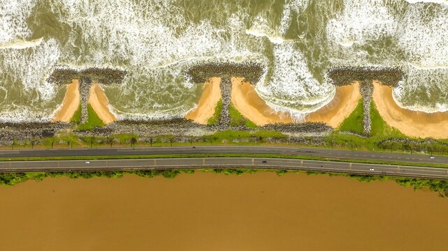 Aerial view of Maravanthe beach featuring a road separating the Arabian Sea and the Souparnika River, with T-shaped groynes and sandy coastline in Maravanthe, Karnataka, India.