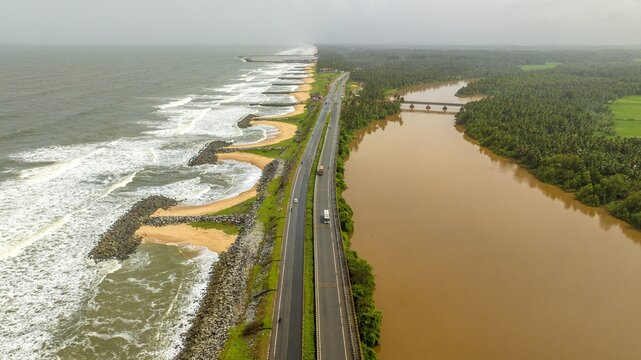 Aerial view of Maravanthe beach with the Arabian Sea and Souparnika River separated by a highway, lush palm trees, and coastal infrastructure in Maravanthe, Karnataka, India.
