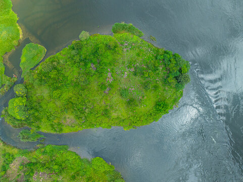 Aerial view of a lush green island surrounded by the flowing waters of the River Nile, featuring dense vegetation and rocky outcrops in Jinja, Eastern Region, Uganda.