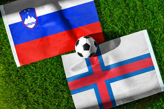 Slovenia vs. Faroe Islands football match. National flags on green grass with soccer ball in the middle. Football background for international match.