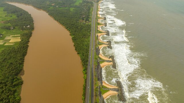 Aerial view of Maravanthe beach with the Arabian Sea on one side and the Suparnika River on the other, separated by a highway in Maravanthe, Karnataka, India.