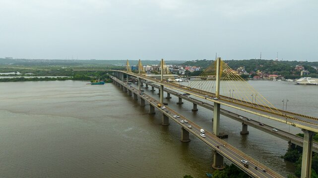 Aerial view of the Atal Setu bridge spanning the Mandovi River with traffic flowing across the cable-stayed structure and lush greenery along the riverbanks in Panaji, Goa, India.