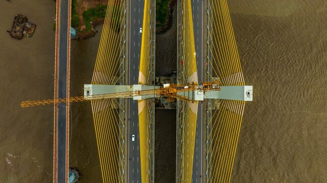 Aerial view of the Zuari Bridge with its distinctive yellow cables and a construction crane positioned over the river in Cortalim, Goa, India.