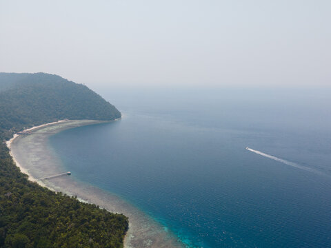 Aerial view of Kri Island surrounded by turquoise coral reefs and deep blue sea with a small boat leaving a wake in Raja Ampat, Southwest Papua, Indonesia.