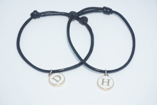Pair of matching black couple bracelets with initial D and H pendants isolated on white background