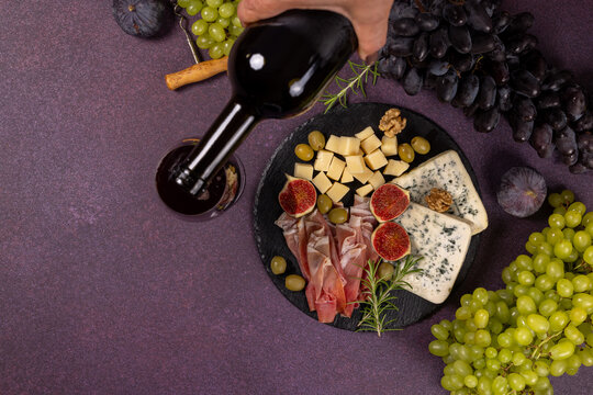 Pouring red wine into glass with charcuterie board