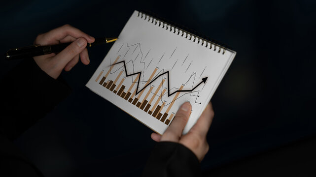 A person holds a sketchbook featuring graphs that illustrate trends and fluctuations in stock market data, symbolizing financial growth and strategic analysis. Scalp