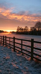 Fototapeta premium a serene sunrise over a frosty field. The sky is a gradient of orange, pink, and blue, with wispy clouds scattered across the horizon. The sun casts a warm glow over the scene.