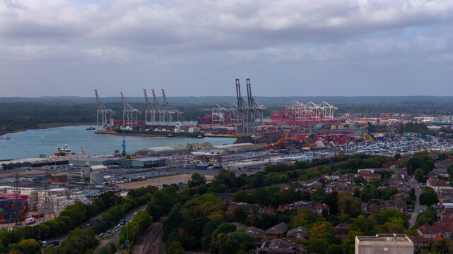 Aerial view of the busy Port of Southampton featuring large container ships, towering cranes, and extensive rows of parked vehicles along the waterfront in Southampton, England, United Kingdom.