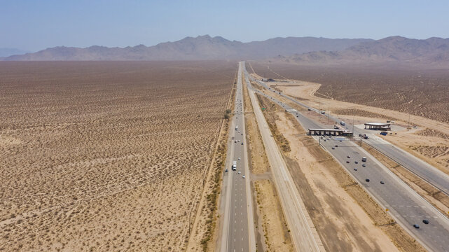Aerial view of a highway stretching through a vast arid desert landscape with mountains in the background and a toll booth facility in the United States.