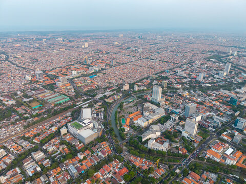 Aerial view of the dense urban landscape of Surabaya with high-rise buildings, a winding river, and residential rooftops in Surabaya, East Java, Indonesia.