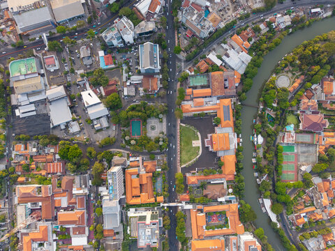 Aerial view of the urban landscape in Surabaya featuring dense buildings with orange rooftops, a winding river, lush green trees, and busy roads in Surabaya, East Java, Indonesia.