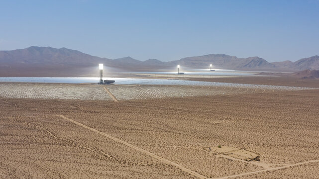 Aerial view of a large concentrated solar power plant with thousands of mirrors and central solar towers in a desert landscape in the United States.