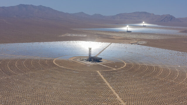 Aerial view of a concentrated solar power plant with thousands of heliostat mirrors surrounding a central solar tower in a vast desert landscape, United States.