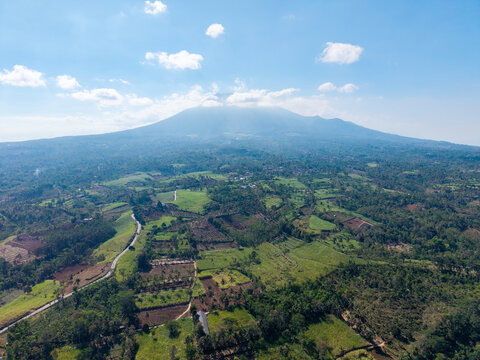 Aerial view of the lush green landscape and agricultural fields surrounding the mountain in Ngajum, East Java, Indonesia.