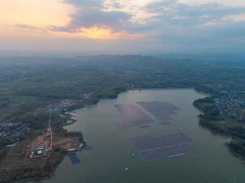 Aerial view of Sutami Dam at Karangkates with floating solar panel arrays on the reservoir surface surrounded by hills at sunset in Kecamatan Sumberpucung, Jawa Timur, Indonesia.