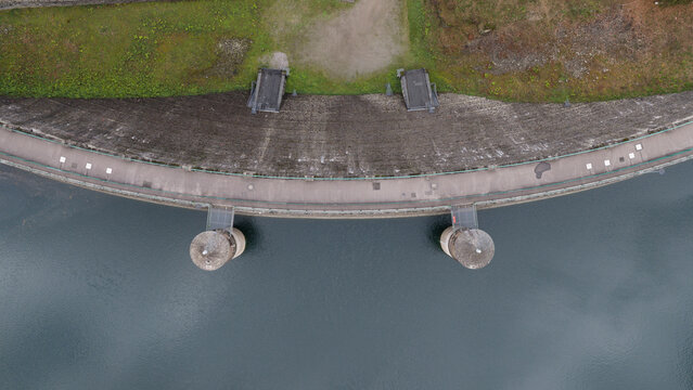 Aerial view of Sengbachtalsperre dam wall with its distinctive curved structure, water reservoir, and two circular intake towers in Solingen, Nordrhein-Westfalen, Germany.