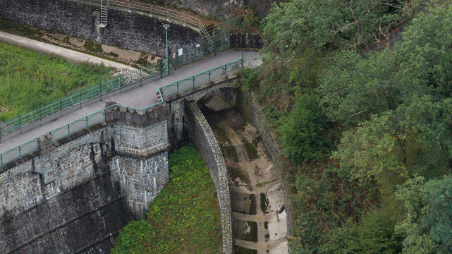 Aerial view of Sengbachtalsperre dam structure featuring a stone bridge, concrete spillway, and surrounding lush forest in Solingen, Nordrhein-Westfalen, Germany.