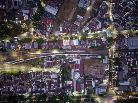 Aerial view of the city of Malang at night, featuring illuminated streets, dense residential rooftops, and railway tracks running through the urban landscape in Malang, East Java, Indonesia.