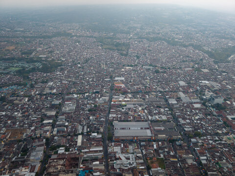 Aerial view of the dense urban landscape of Malang featuring numerous residential rooftops, commercial buildings, and intersecting streets in Malang, East Java, Indonesia.