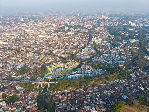 Aerial view of the vibrant Jodipan Colorful Village with its brightly painted houses situated along the river and railway bridge in the dense urban landscape of Malang, East Java, Indonesia.