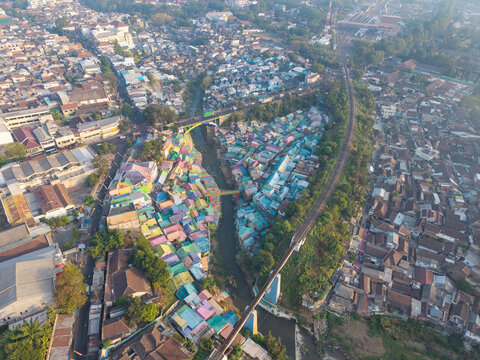 Aerial view of Jodipan Colorful Village with vibrant houses along the river and a railway bridge in Malang, East Java, Indonesia.