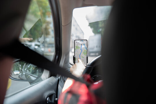 Driver touches a smartphone navigation map mounted beside the steering wheel while traveling. Hand using a mobile GPS application on a phone holder inside a car