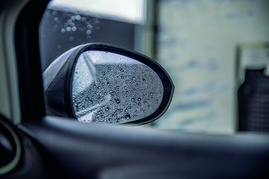 Close-up of water droplets on a vehicle mirror during rain, showing wet road conditions and seasonal weather change, rainfall, reduced visibility and a rainy weather forecast