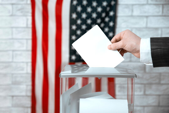 Voter casting a voting ballot into a transparent ballot box with the US flag. American elections, democracy and voting rights.