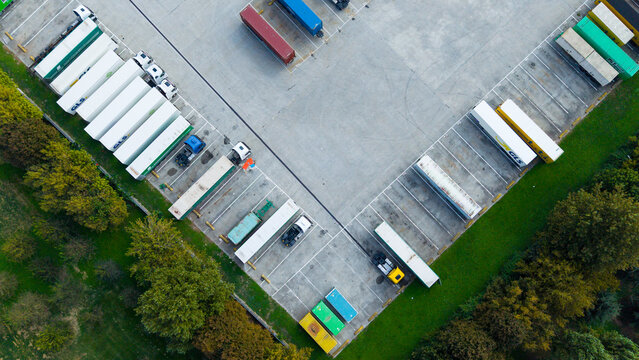 Aerial view of commercial trailers and shipping containers parked in an organized logistics facility surrounded by lush trees in Milan, Lombardy, Italy.
