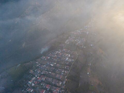 Aerial view of Wonotoro village nestled in the mountains of East Java, partially shrouded in mist during a golden sunset in Sukapura, East Java, Indonesia.