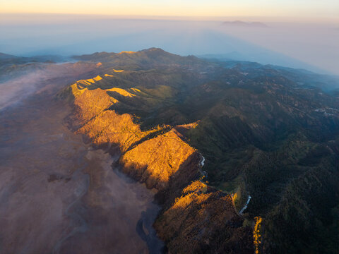 Aerial view of the Podokoyo region near Mount Bromo, featuring rugged volcanic terrain, deep valleys, and golden hour light illuminating the mountain ridges in Tosari, East Java, Indonesia.