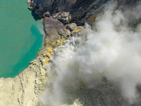 Aerial view of the turquoise acidic crater lake and thick sulfurous smoke rising from the mining site at Mount Ijen, Ijen, East Java, Indonesia.