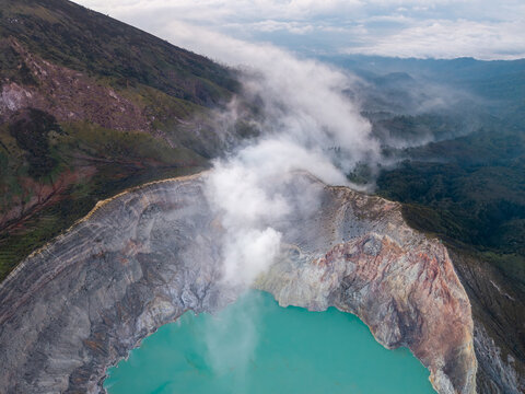 Aerial view of Ijen crater featuring its iconic turquoise acidic lake, rugged volcanic walls, and rising steam plumes set against the mountainous landscape in Ijen, East Java, Indonesia.