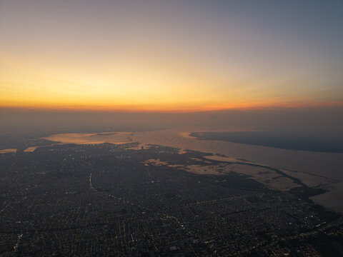 Aerial view of the city of Surabaya at sunset with the coastline and urban sprawl visible under a golden sky, Surabaya, East Java, Indonesia.