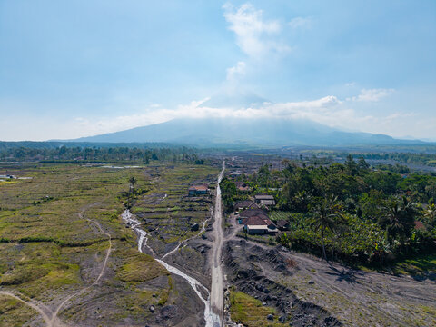 Aerial view of the volcanic landscape near Mount Semeru, showing the aftermath of a catastrophic eruption with ash-covered fields and rural houses in Pronojiwo, East Java, Indonesia.