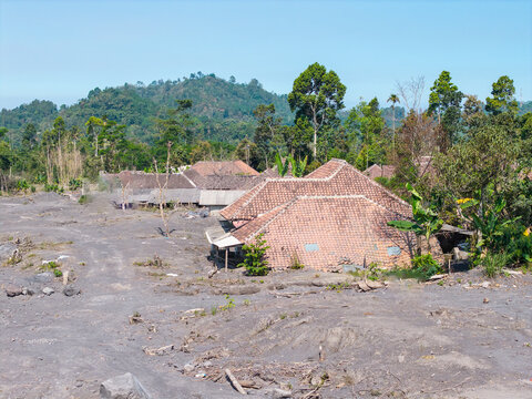 Aerial view of the aftermath of the Mount Semeru eruption in Supiturang Village, showing houses buried in volcanic ash and debris near lush tropical vegetation, Pronojiwo, East Java, Indonesia.