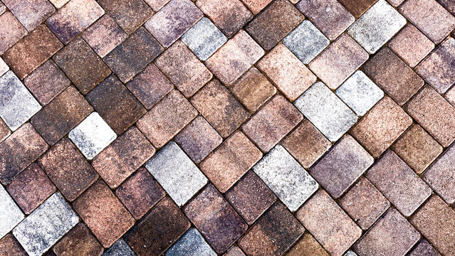 interlocking rectangular stone pavers in shades of brown grey and tan form a textured diagonal herringbone pavement pattern