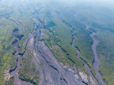 Aerial view of the volcanic landscape showing the aftermath of Mount Semeru eruption with dark ash deposits cutting through lush green vegetation in Pronojiwo, East Java, Indonesia.