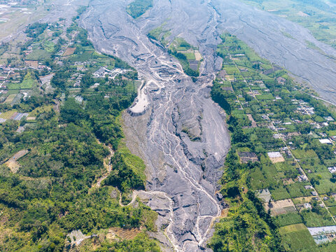 Aerial view of volcanic debris flow from Mount Semeru covering the landscape near Supiturang Village, with ash deposits contrasting against green fields in Pronojiwo, East Java, Indonesia.