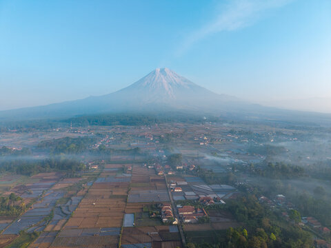 Aerial view of Mount Semeru rising above the misty agricultural fields and village of Sumberurip in Pronojiwo, East Java, Indonesia.