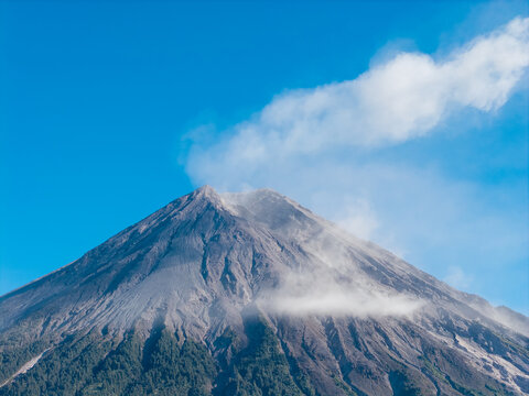 Aerial view of the volcanic peak of Mount Semeru with smoke rising into a clear blue sky above the forested slopes in Pasrujambe, East Java, Indonesia.