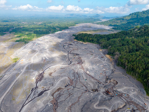 Aerial view of the lava path of Mount Semeru with volcanic debris, heavy machinery, and surrounding tropical forest in Candipuro, East Java, Indonesia.