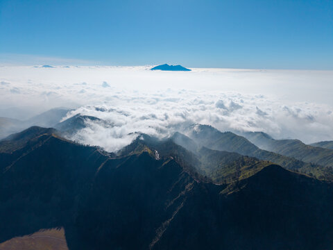Aerial view of the mountainous landscape of Mount Bromo area with a thick sea of clouds and clear blue sky in Kecamatan Tosari, Jawa Timur, Indonesia.