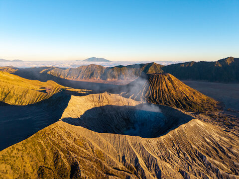 Aerial view of Mount Bromo with its smoking volcanic crater and rugged landscape illuminated by golden hour light in Tosari, East Java, Indonesia.