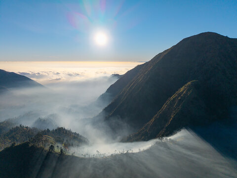Aerial view of the mountainous landscape with mist-filled valleys and dramatic sunlight illuminating the peaks in Sukapura, East Java, Indonesia.