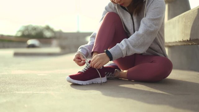 Running shoes with red laces stand on pavement beside a waterfront path. The running shoes fill the frame above athletic feet, with crossed shoelaces, a metal railing, and water beyond the path.