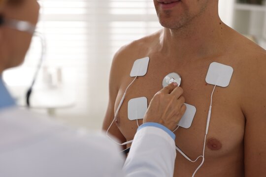 Cardiologist with stethoscope listening to patient's heartbeat during ECG test in clinic, closeup