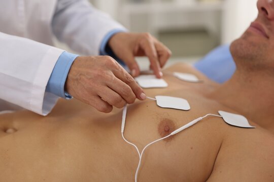 Doctor attaching ECG electrodes to patient's chest in clinic, closeup