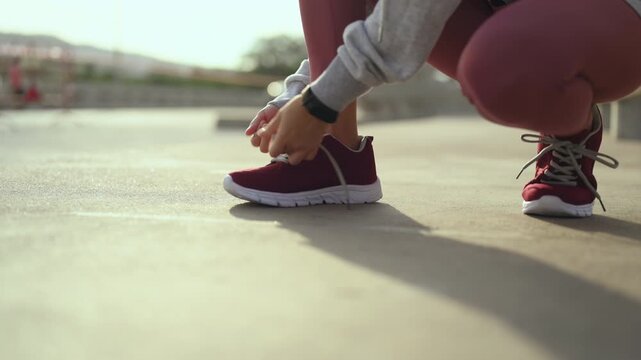 Running shoes with red laces stand on pavement beside a waterfront path. The running shoes fill the frame above athletic feet, with crossed shoelaces, a metal railing, and water beyond the path.